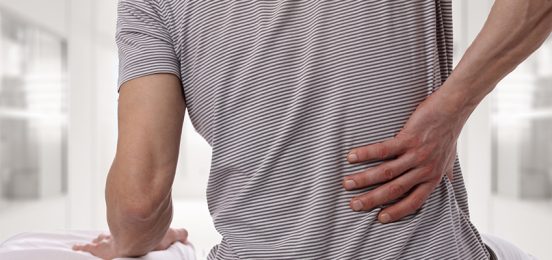 Man suffering from back pain at home in the bedroom. Uncomfortable mattress and pillow causes back pain.